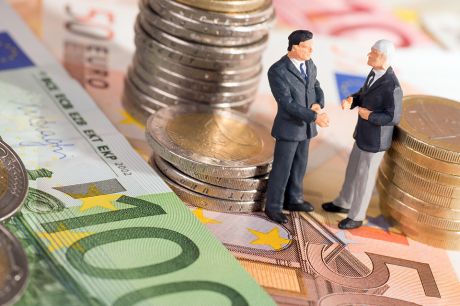 Foto: Zwei kleine Figuren stehend auf Geldscheine umringt von Münzen 